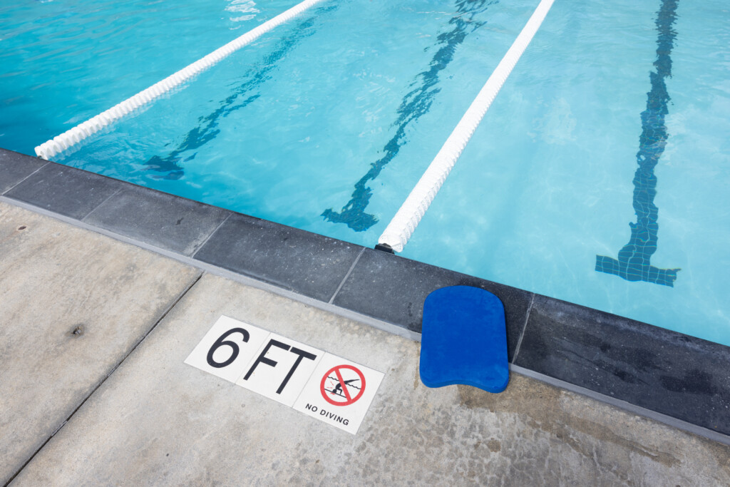 Swimming pool with lane dividers, a blue kickboard on the edge, and a sign indicating 6 feet depth and no diving.