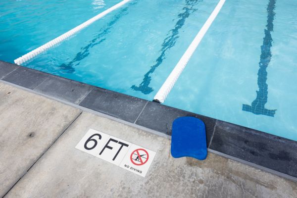 Swimming pool with lane dividers, a blue kickboard on the edge, and a sign indicating 6 feet depth with a no diving symbol.
