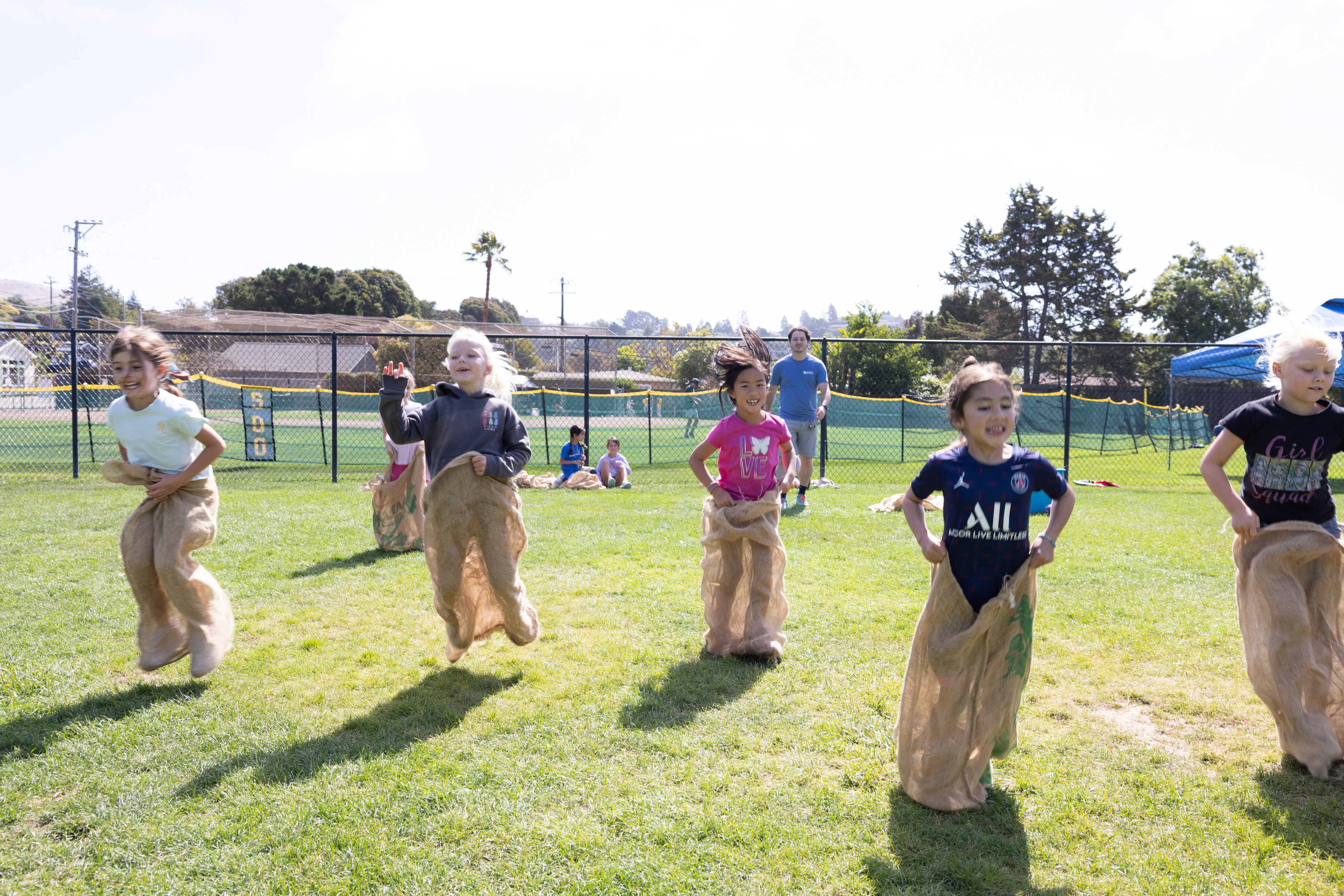 5 kids on a field hopping, racing in burlap bags