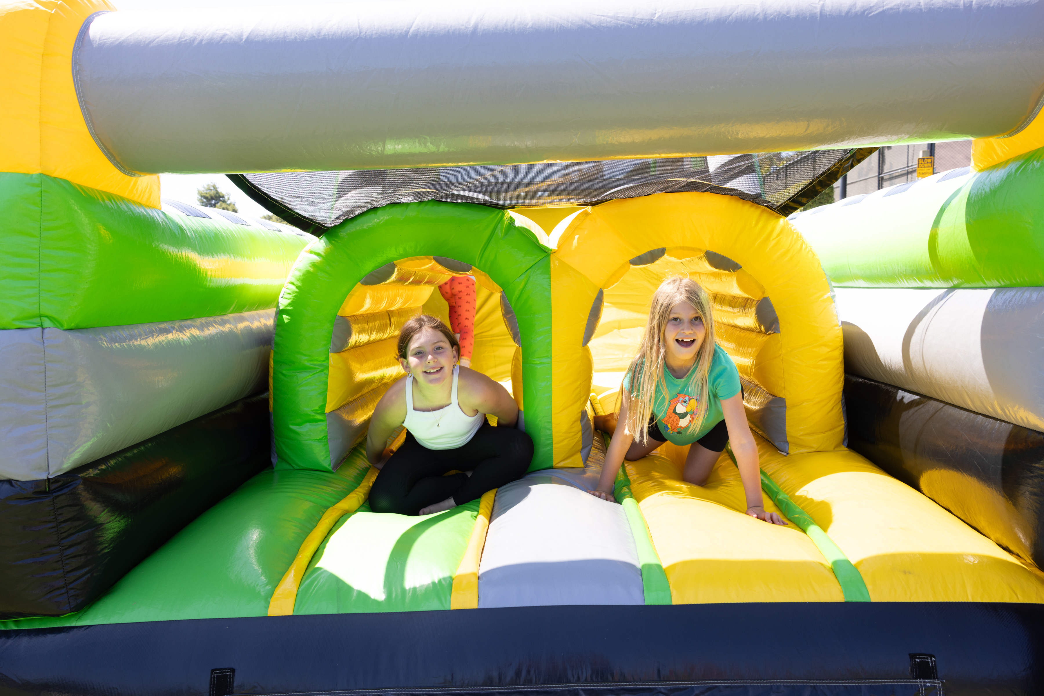 Two children crawl out of tunnels in a brightly colored inflatable obstacle course on a sunny day.