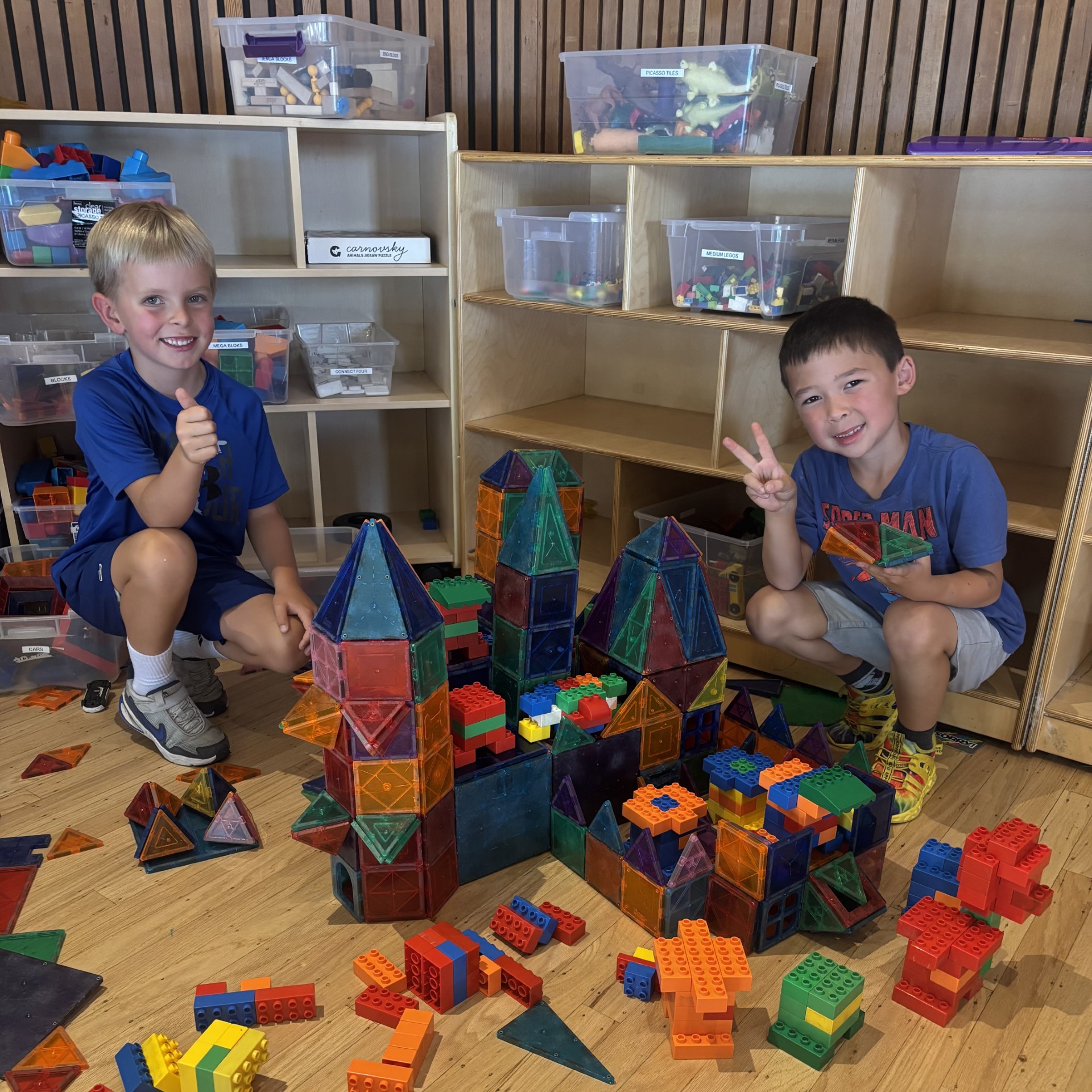 Two young boys posing for the camera in front of their creation made of tiles