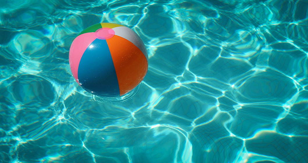 A colorful inflatable beach ball floats on clear blue water in a swimming pool, casting reflections on the surface.